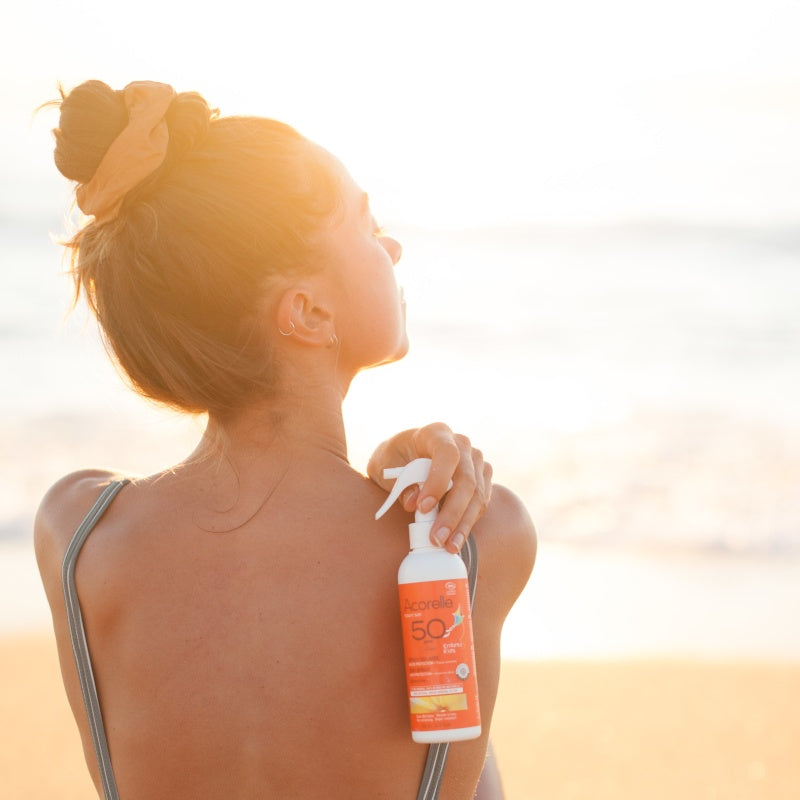 Spray solaire enfants SPF50 tenu par une femme sur la plage