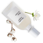 Flacon rechargeable Musc & Coton Veronika Loubry posé sur une branche de Coton et une fleur blanche