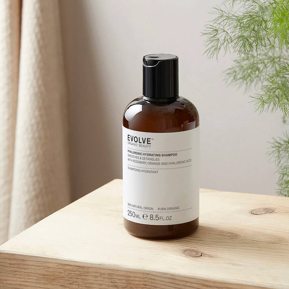 Flacon du shampoing bio pour cheveux secs à l'Acide Hyaluronique Evolve Beauty posé sur une table en bois près d'une plante